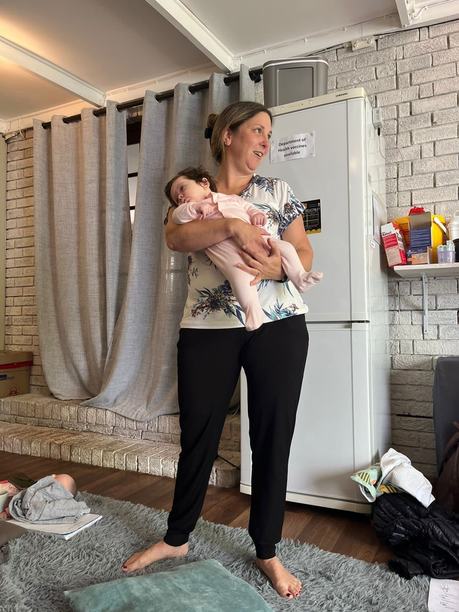 Megan holding a baby at the clinic with a vaccine information sign